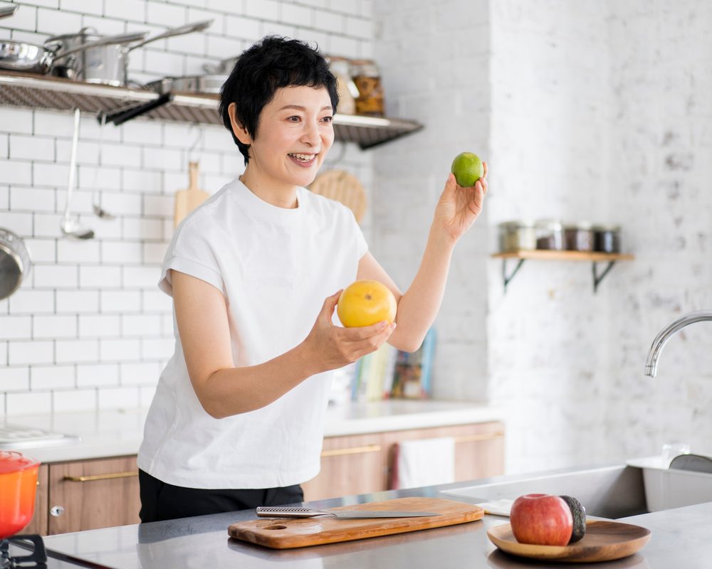 短发女性在明亮的厨房里手拿柚子和青柠，准备做饭（模特摆拍）