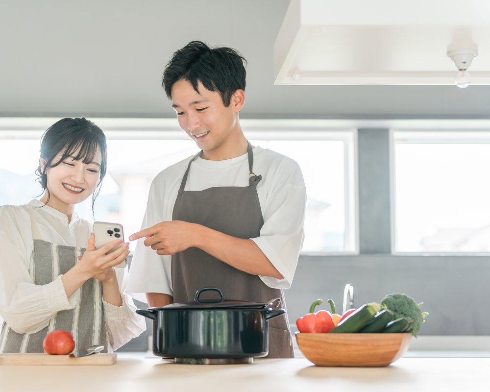 年轻夫妻在厨房一起做饭、看手机(模特摆拍)
